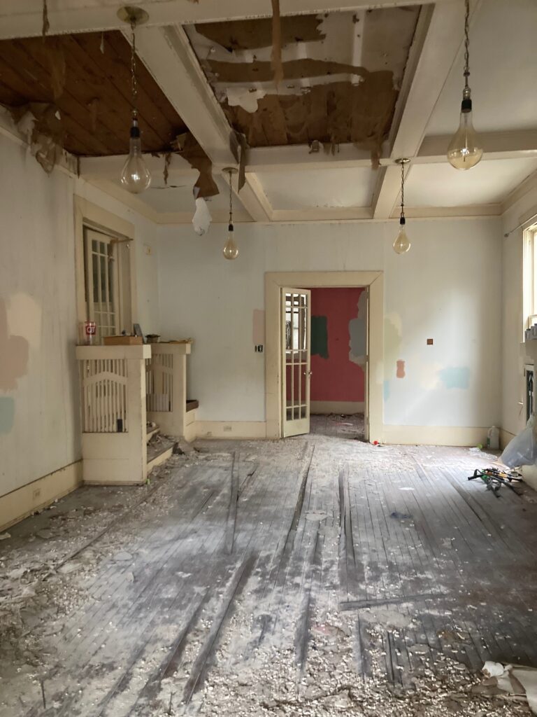 Fire-damaged living room with an open ceiling, affected flooring, and original fireplace built-ins.