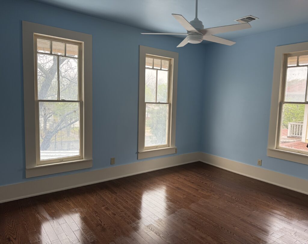 Restored blue bedroom with wood flooring, white trim, and a ceiling fan.