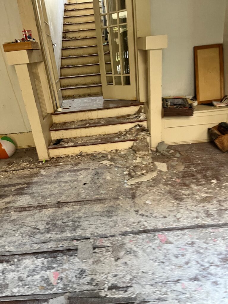 Stair entrance before restoration with damaged flooring and debris.