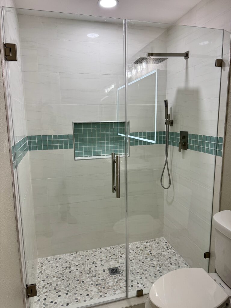 Glass-enclosed shower with white wall tile, a green tile accent band, recessed storage and a mosaic floor.