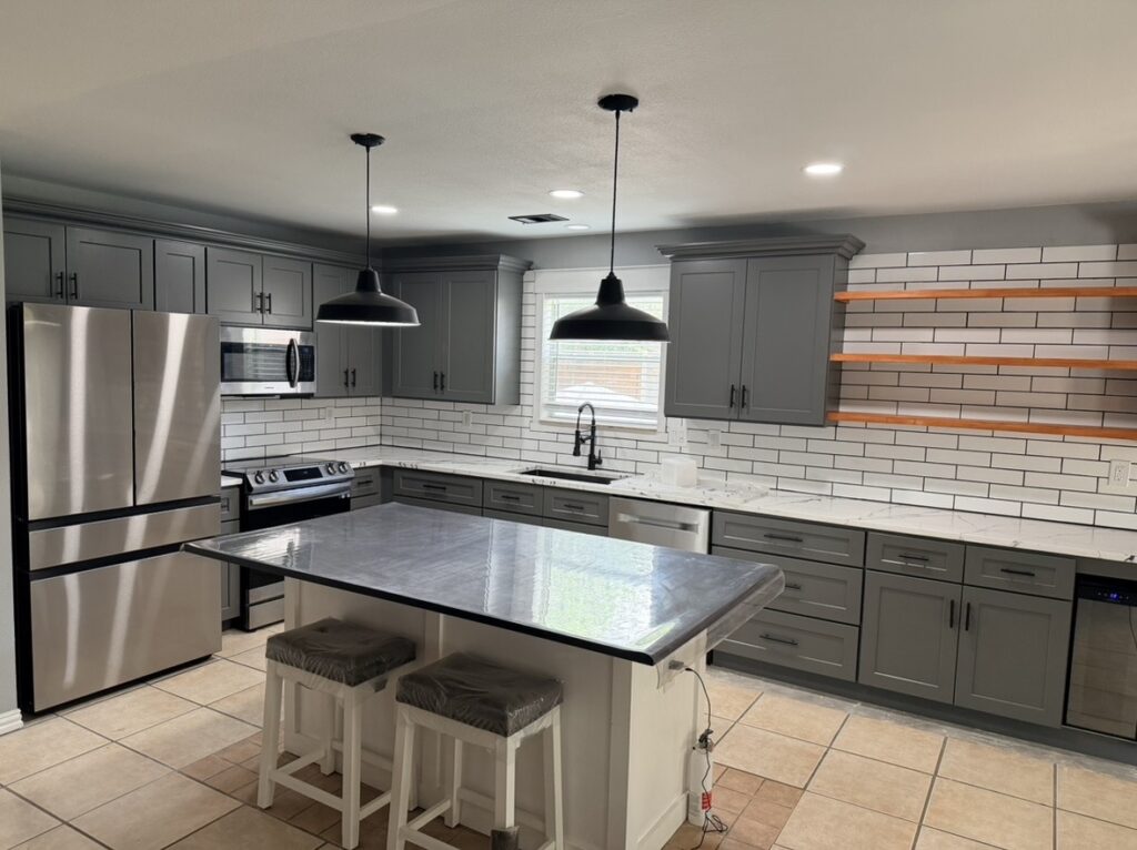 Gray kitchen cabinets surrounding a central island with two stools and pendant lights.