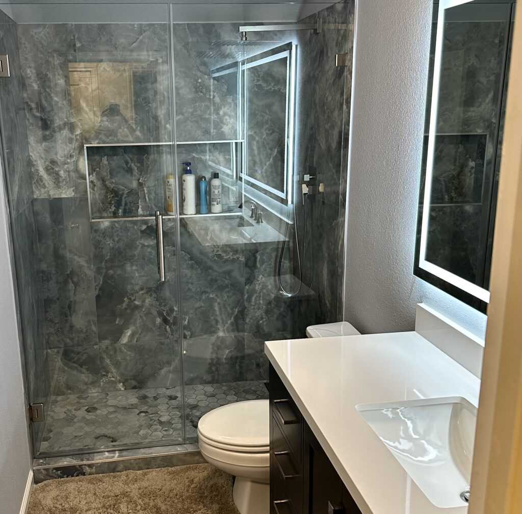 Bathroom with a glass shower enclosure, toilet and compact vanity arranged along one wall.