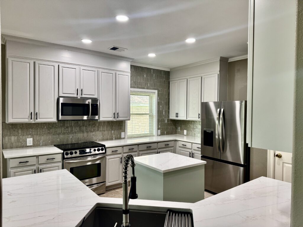 White upper and lower kitchen cabinets around stainless steel appliances, with light countertops and a tile backsplash.