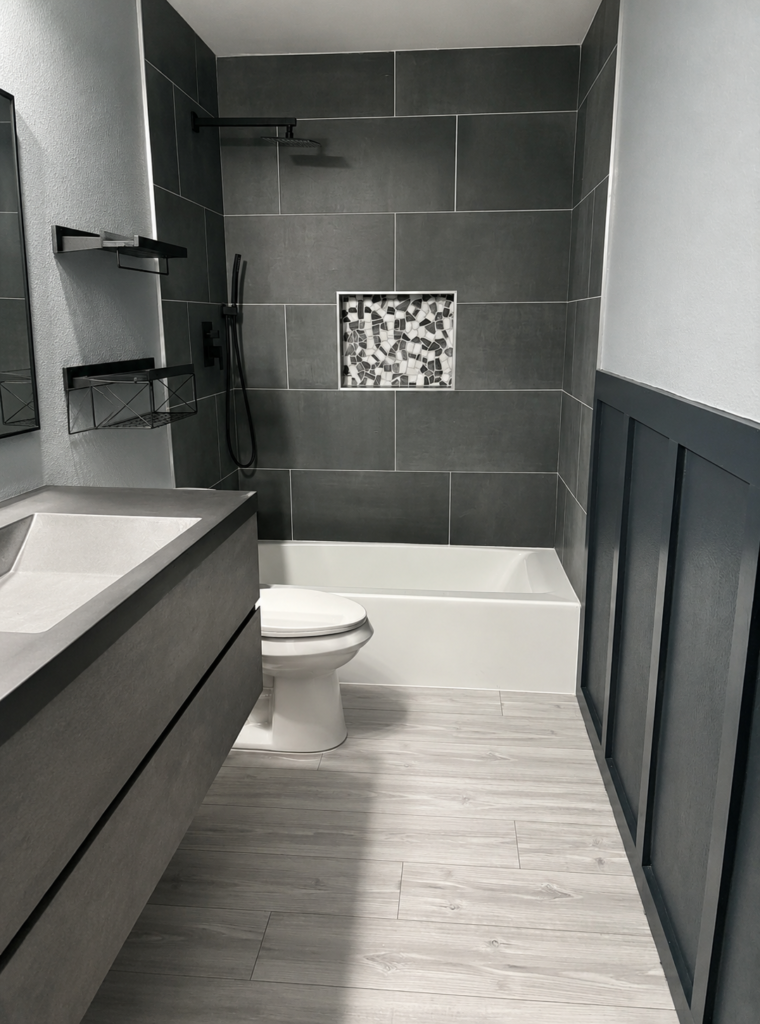 Finished bathroom with a white bathtub, glass screen, dark tiled surround, mosaic niche and vanity.