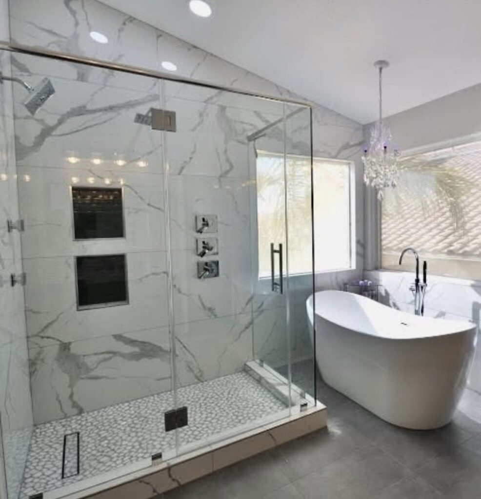 Bathroom with marble-look wall tile, a glass shower enclosure, and a freestanding white bathtub.
