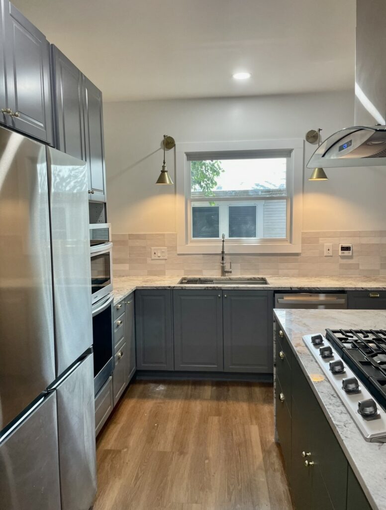 Gray kitchen cabinets, an island cooktop, light counters, stainless steel appliances and brass-tone wall lights.