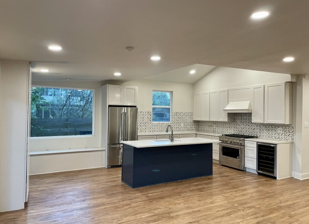 White kitchen cabinets, a dark island, patterned backsplash, recessed lighting and wood flooring.