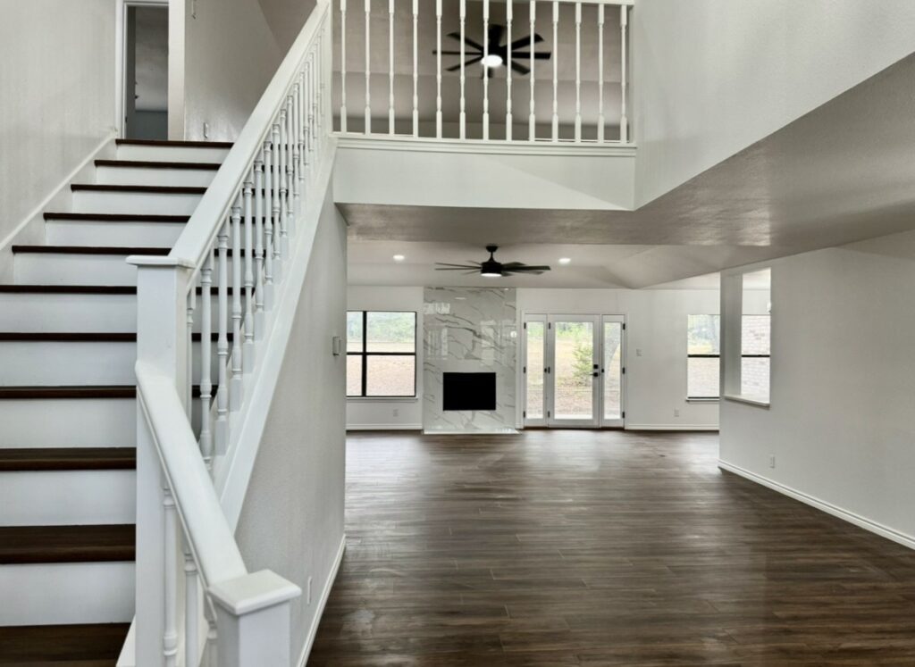 Open living area with white stair railings, wood-tone flooring, a fireplace and rear glass doors.