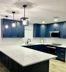 Deep blue kitchen cabinets, light mosaic tile and a white peninsula beneath three pendant lights.