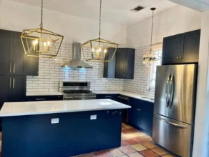 Navy kitchen cabinets, white subway tile, a light island countertop and geometric gold-tone pendant lights.