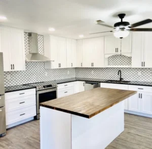 White kitchen cabinets, a black-and-white patterned backsplash and a wood-topped island.