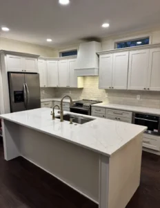 White kitchen cabinetry and island with brass-tone fixtures, light counters and a white range hood.