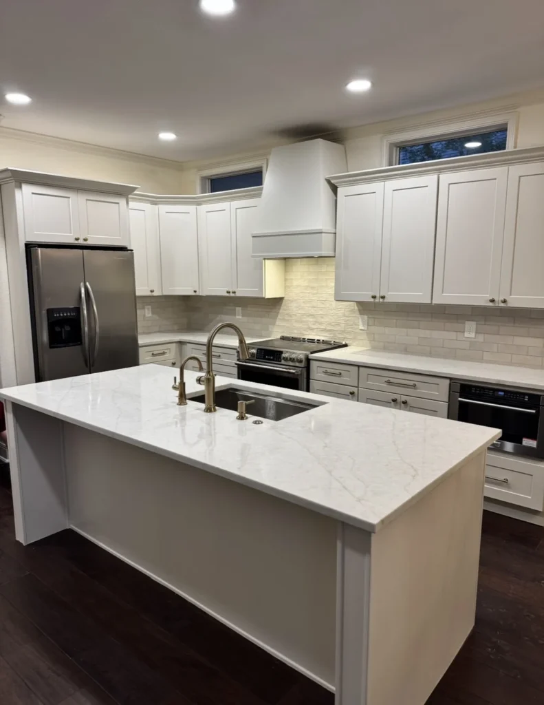 White kitchen cabinetry and island with brass-tone fixtures, light counters and a white range hood.