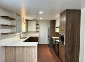 Kitchen with wood-grain cabinets, white upper cabinets and counters, open wood shelves and terracotta-colored floor tile.